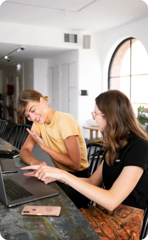 Deux femmes discutant avec enthousiasme devant leurs ordinateurs, collaborant sur des concepts UX et UI design basés sur le Design Thinking et la créativité.