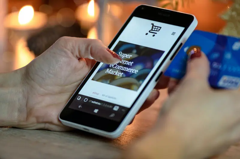 Main tenant un téléphone, avec l'autre main tenant une carte bancaire, symbolisant le processus de paiement en ligne pour améliorer la conversion d'un site web.