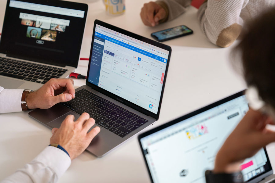 Des personnes concentrées sur leurs ordinateurs et téléphones, travaillant sur une webapp, mettant en avant l'utilisation de solutions numériques efficaces dans les projets d'Ethiko.