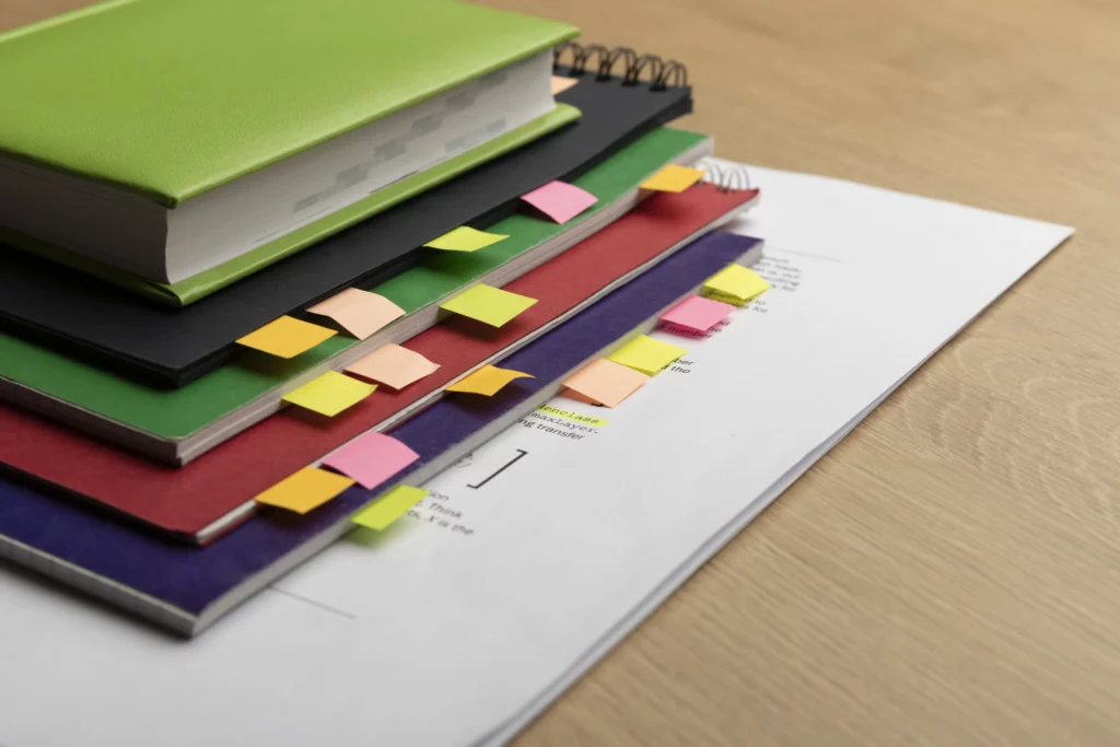 Pile de cahiers et documents avec des marque-pages colorés posés sur un bureau pour faire des cahier des charges d'un site web