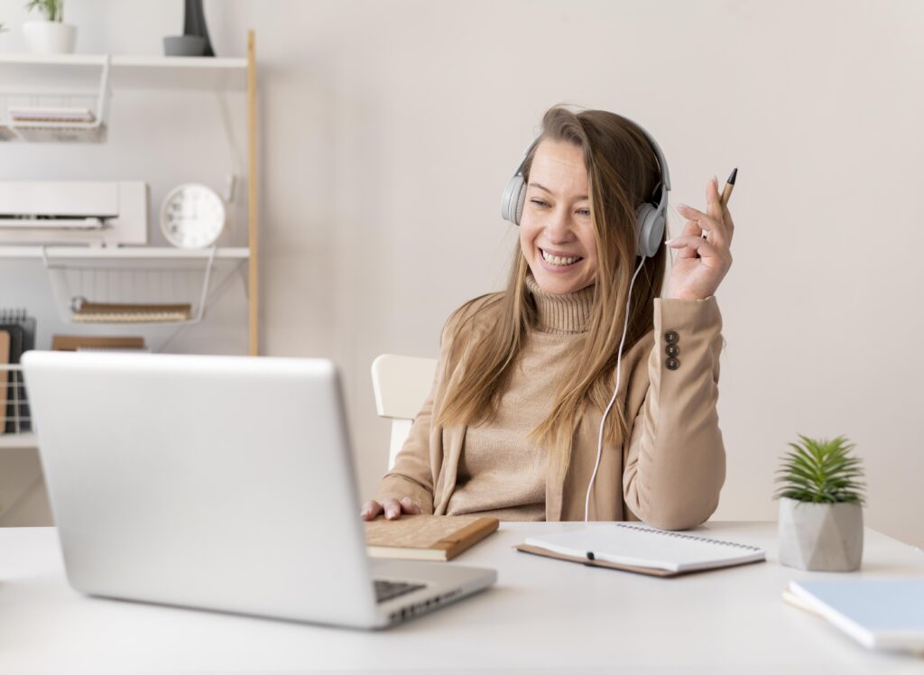 Femme souriante portant un casque audio, assise à son bureau devant un ordinateur portable lors d’une formation en ligne très clair
